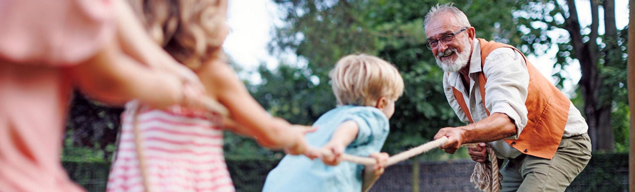 Children playing rope game with grand father in park.