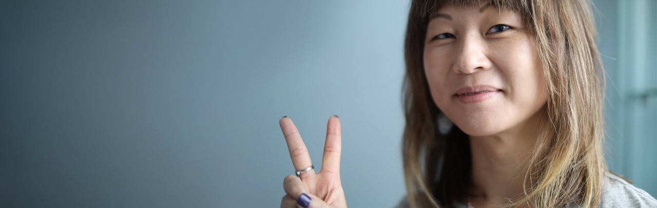 Younger Asian American woman smiling confidently, holding her hand in a peace sign.